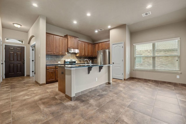 18712 Leigh Ln, Pflugerville, TX 78660 - kitchen with freestanding refrigerator, a kitchen bar, tasteful backsplash, brown cabinetry, and under cabinet range hood