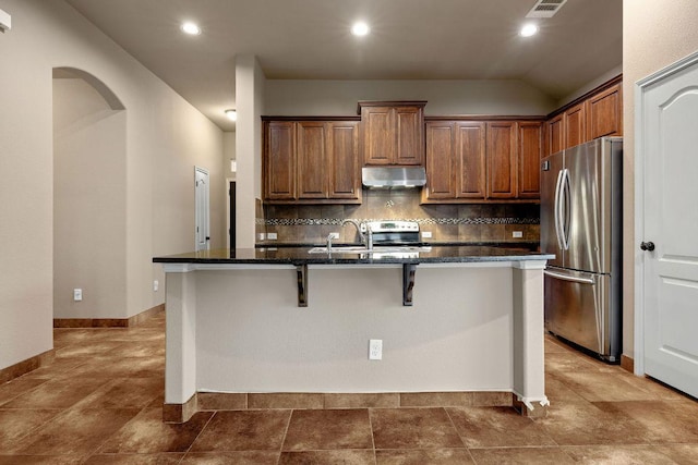 18712 Leigh Ln, Pflugerville, TX 78660 - kitchen with freestanding refrigerator, under cabinet range hood, a kitchen breakfast bar, tasteful backsplash, and an island with sink
