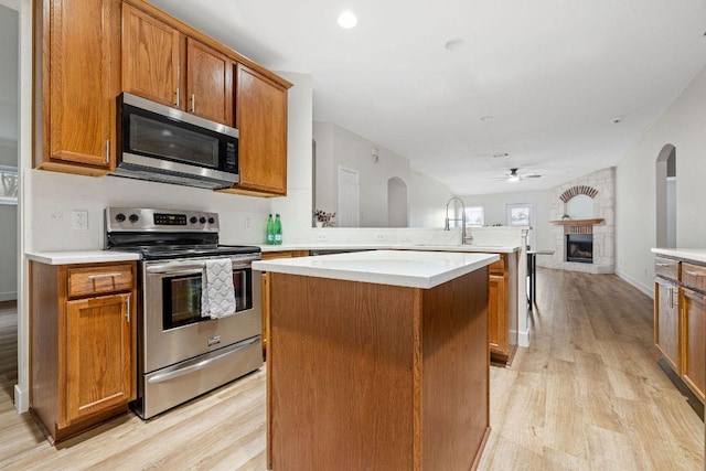 608 Timothy John Dr, Pflugerville, TX 78660 - kitchen with appliances with stainless steel finishes, a peninsula, light wood-style flooring, a kitchen island, and a fireplace