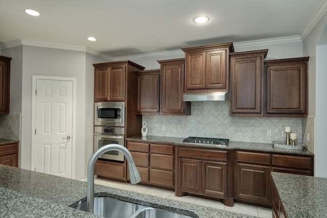 12421 Black Hills Dr, Austin, TX 78748 - kitchen with appliances with stainless steel finishes, dark stone counters, decorative backsplash, under cabinet range hood, and ornamental molding