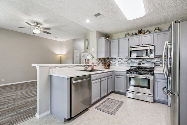17003 Jigsaw Pathway, Round Rock, TX 78664 - kitchen with appliances with stainless steel finishes, gray cabinets, a textured ceiling, tasteful backsplash, and a peninsula