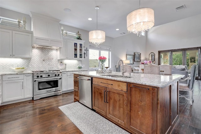 3973 River Place Blvd, Austin, TX 78730 - kitchen featuring appliances with stainless steel finishes, a chandelier, white cabinetry, tasteful backsplash, and a center island with sink