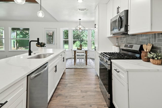 2207 Emerald Isle Dr, Leander, TX 78641 - kitchen featuring stainless steel appliances, light wood finished floors, white cabinets, and decorative light fixtures