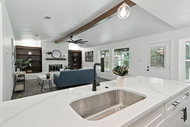 2207 Emerald Isle Dr, Leander, TX 78641 - kitchen with a ceiling fan, light stone countertops, wood finished floors, white cabinetry, and a stone fireplace
