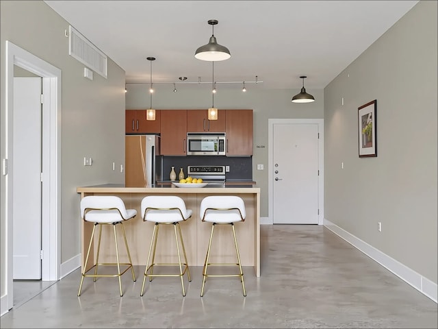 3016 Guadalupe St Unit 211, Austin, TX 78705 - kitchen featuring appliances with stainless steel finishes, brown cabinets, concrete floors, a kitchen breakfast bar, and decorative light fixtures