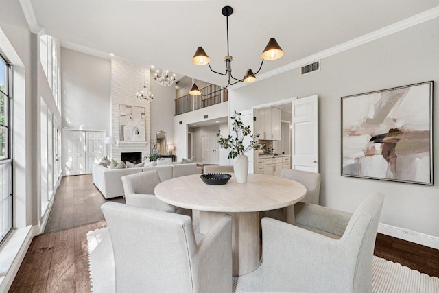 7204 Guava Cv, Austin, TX 78750 - dining space with a chandelier, crown molding, dark wood-style flooring, a high ceiling, and a large fireplace