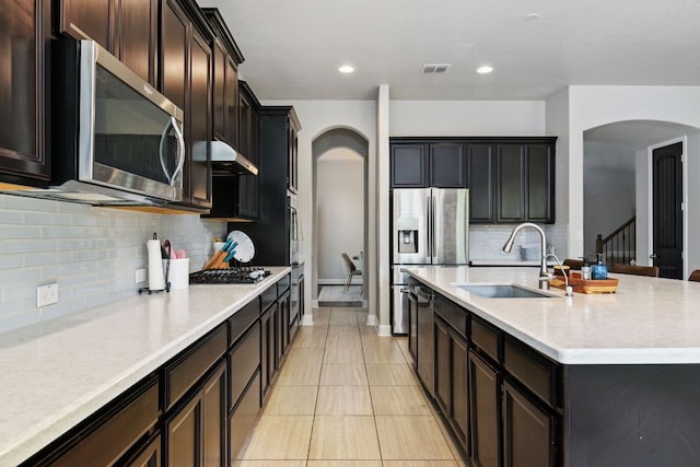 30872 Schlather Ln, Bulverde, TX 78163 - kitchen featuring appliances with stainless steel finishes, arched walkways, an island with sink, light countertops, and under cabinet range hood