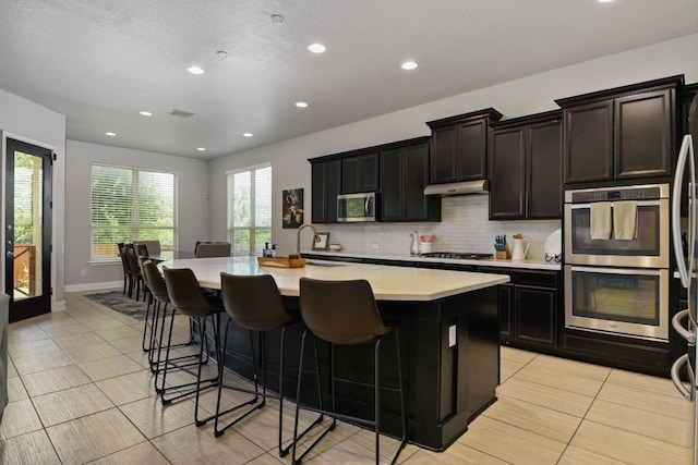 30872 Schlather Ln, Bulverde, TX 78163 - kitchen featuring appliances with stainless steel finishes, light countertops, light tile patterned floors, a kitchen island with sink, and recessed lighting