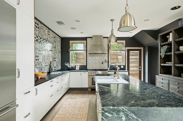 913 Christopher St, Austin, TX 78704 - kitchen featuring wall chimney exhaust hood, stainless steel appliances, dark countertops, wood finished floors, and white cabinets