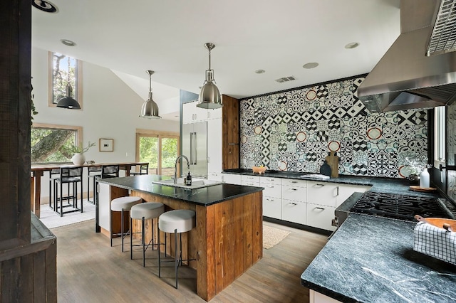 913 Christopher St, Austin, TX 78704 - kitchen featuring ventilation hood, dark countertops, wood finished floors, a kitchen bar, and white cabinets