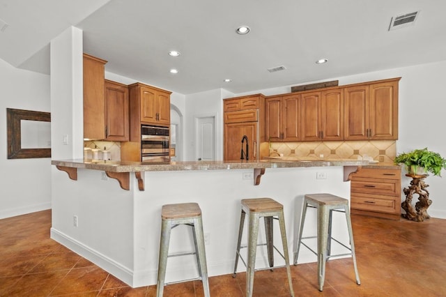 9 Heatherbloom Ln, The Hills, TX 78738 - kitchen with a kitchen breakfast bar, recessed lighting, tasteful backsplash, brown cabinets, and double oven