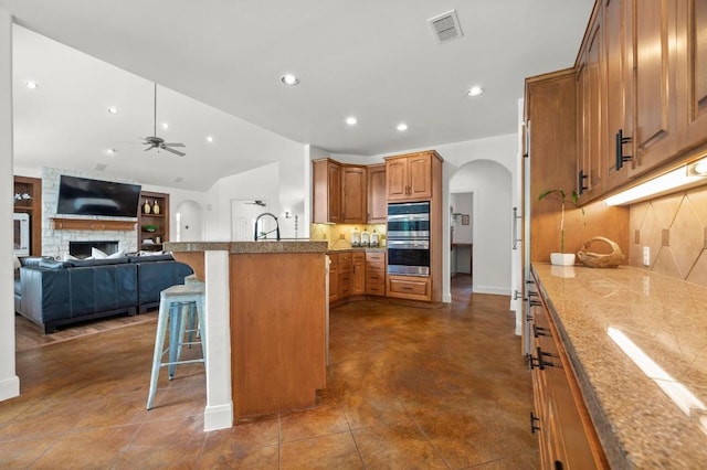 9 Heatherbloom Ln, The Hills, TX 78738 - kitchen with arched walkways, a breakfast bar area, ceiling fan, recessed lighting, and brown cabinetry