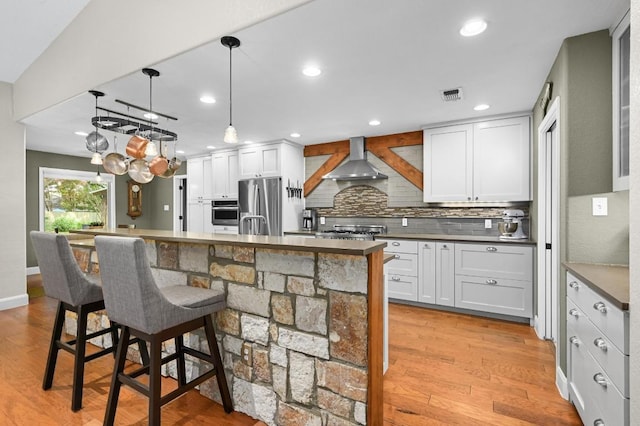 2400 Muirfield Cir, Austin, TX 78747 - kitchen with wall chimney exhaust hood, appliances with stainless steel finishes, decorative backsplash, a breakfast bar, and light wood-type flooring