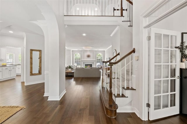 11235 Tracton Ln, Austin, TX 78739 - entrance foyer featuring stairway, crown molding, dark wood finished floors, arched walkways, and a warm lit fireplace