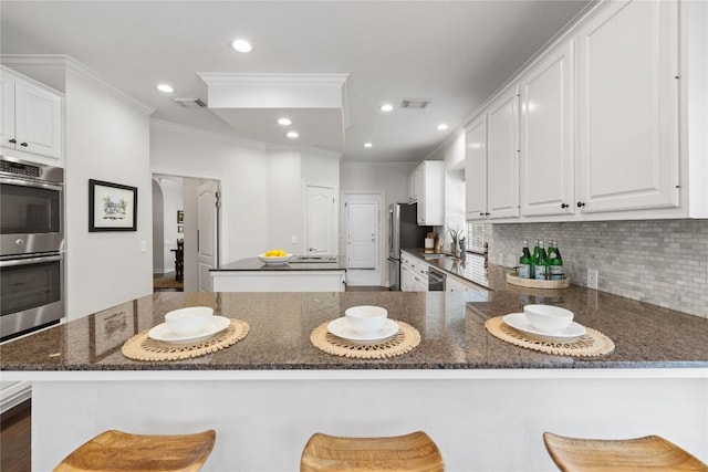 11235 Tracton Ln, Austin, TX 78739 - kitchen featuring appliances with stainless steel finishes, crown molding, white cabinets, tasteful backsplash, and a peninsula
