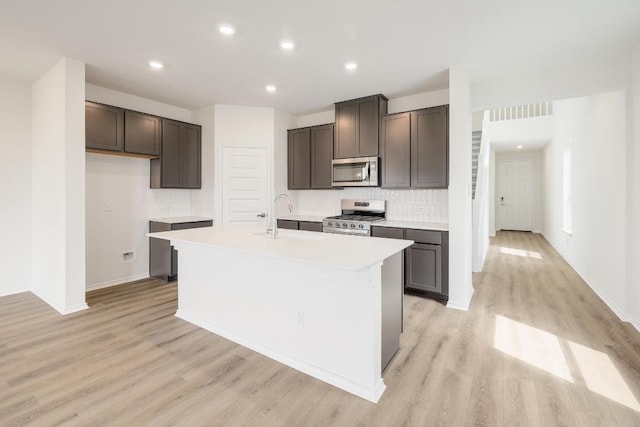 4935 Mozzafiato Ln, Round Rock, TX 78665 - kitchen featuring gas range, stainless steel microwave, light wood-type flooring, a center island with sink, and backsplash