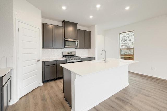 4935 Mozzafiato Ln, Round Rock, TX 78665 - kitchen featuring stainless steel appliances, light wood finished floors, tasteful backsplash, a kitchen island with sink, and light countertops
