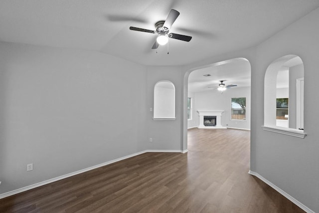 8943 W Hove Loop, Austin, TX 78749 - unfurnished room featuring ceiling fan, dark wood-type flooring, a fireplace with raised hearth, and arched walkways