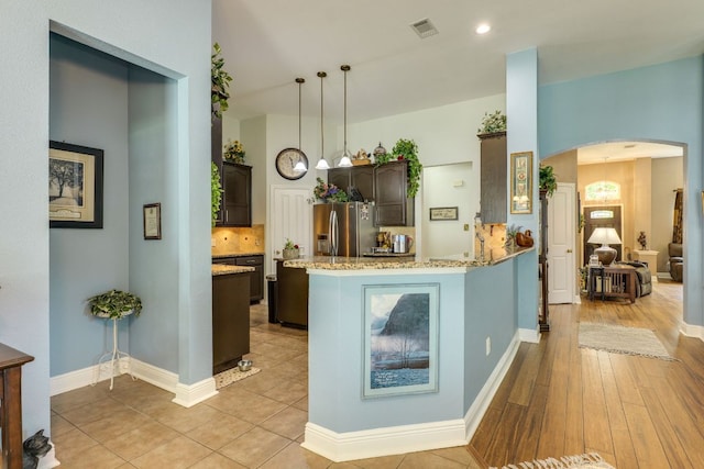 307 N Rainbow Bridge Dr, Cedar Park, TX 78613 - kitchen featuring stainless steel fridge with ice dispenser, arched walkways, dark brown cabinetry, light wood-style flooring, and a peninsula