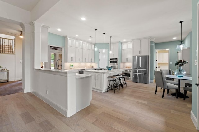 908 Lakewood Hills Ter, Austin, TX 78732 - kitchen with stainless steel appliances, a breakfast bar area, light wood-type flooring, white cabinetry, and light countertops