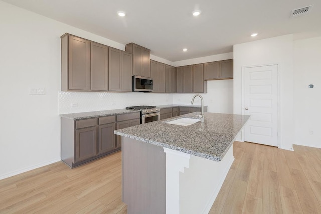 4852 Mozzafiato Ln, Round Rock, TX 78665 - kitchen with stainless steel appliances, light wood finished floors, light stone countertops, an island with sink, and recessed lighting
