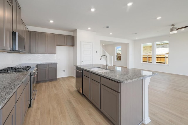 4852 Mozzafiato Ln, Round Rock, TX 78665 - kitchen with stainless steel appliances, light wood finished floors, light stone counters, a center island with sink, and recessed lighting
