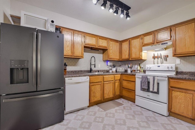 902 Linden St, Bastrop, TX 78602 - kitchen featuring white appliances, under cabinet range hood, light flooring, dark countertops, and decorative backsplash