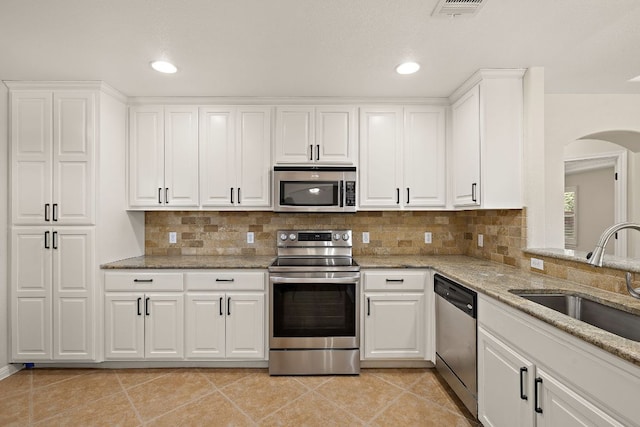 3608 Rockefeller Cv, Lago Vista, TX 78645 - kitchen featuring stainless steel appliances, arched walkways, white cabinetry, light stone countertops, and backsplash