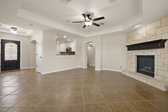 3608 Rockefeller Cv, Lago Vista, TX 78645 - unfurnished living room with a raised ceiling, arched walkways, a ceiling fan, ornamental molding, and a stone fireplace