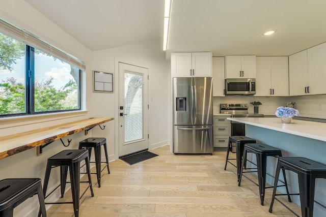 6904 Rusty Fig Dr, Austin, TX 78750 - kitchen with appliances with stainless steel finishes, a kitchen breakfast bar, light wood finished floors, vaulted ceiling, and white cabinets