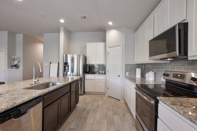 21510 Paine Ave, Lago Vista, TX 78645 - kitchen featuring stainless steel appliances, white cabinetry, decorative backsplash, light wood-type flooring, and light stone countertops