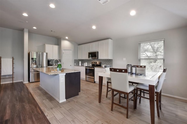 21510 Paine Ave, Lago Vista, TX 78645 - kitchen with stainless steel appliances, decorative backsplash, a kitchen island with sink, vaulted ceiling, and white cabinets