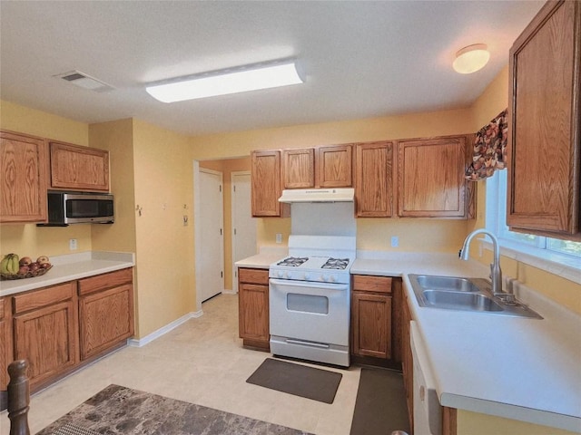 203 Pheasant Trl, Bastrop, TX 78602 - kitchen featuring white gas range oven, under cabinet range hood, stainless steel microwave, and brown cabinets
