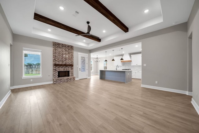 122 Buffalo Ridge Rd, Giddings, TX 78942 - unfurnished living room with a tray ceiling, a ceiling fan, light wood finished floors, a fireplace, and beamed ceiling