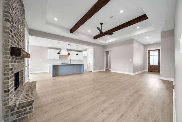 122 Buffalo Ridge Rd, Giddings, TX 78942 - unfurnished living room with a ceiling fan, a brick fireplace, light wood finished floors, beam ceiling, and a raised ceiling