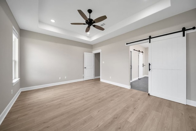 122 Buffalo Ridge Rd, Giddings, TX 78942 - unfurnished bedroom with a barn door, a raised ceiling, light wood-style floors, recessed lighting, and multiple windows