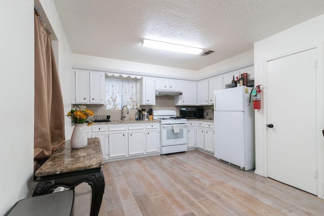 1106 Saucedo St, Austin, TX 78721 - kitchen featuring white appliances, under cabinet range hood, light wood-style floors, white cabinets, and a textured ceiling