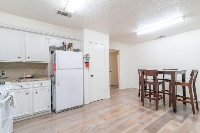 1106 Saucedo St, Austin, TX 78721 - kitchen with white appliances, a textured ceiling, light wood-style floors, white cabinets, and light stone counters