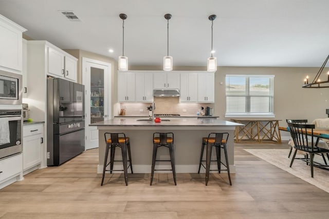 1332 Brescia Walk, Leander, TX 78641 - kitchen featuring appliances with stainless steel finishes, under cabinet range hood, a breakfast bar area, tasteful backsplash, and light wood finished floors