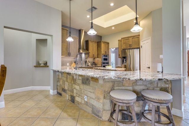 604 Cutty Trl, Lakeway, TX 78734 - kitchen with appliances with stainless steel finishes, wall chimney range hood, brown cabinetry, a peninsula, and backsplash