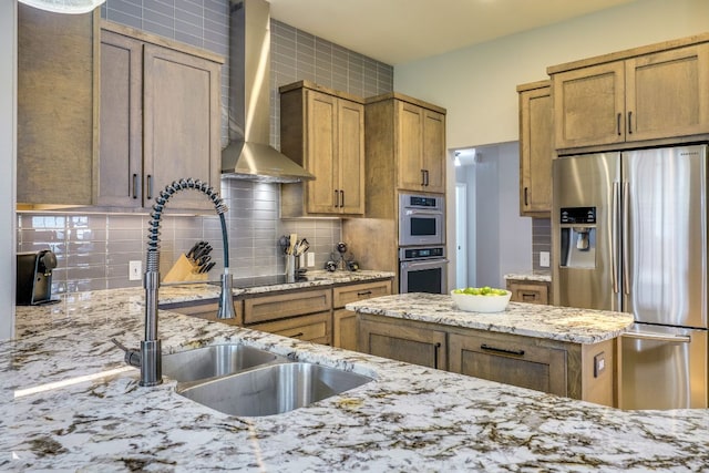 604 Cutty Trl, Lakeway, TX 78734 - kitchen featuring appliances with stainless steel finishes, wall chimney range hood, decorative backsplash, brown cabinetry, and light stone counters