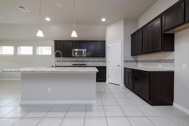 21016 Abigail Way, Pflugerville, TX 78660 - kitchen with stainless steel microwave, backsplash, light stone countertops, light tile patterned flooring, and an island with sink