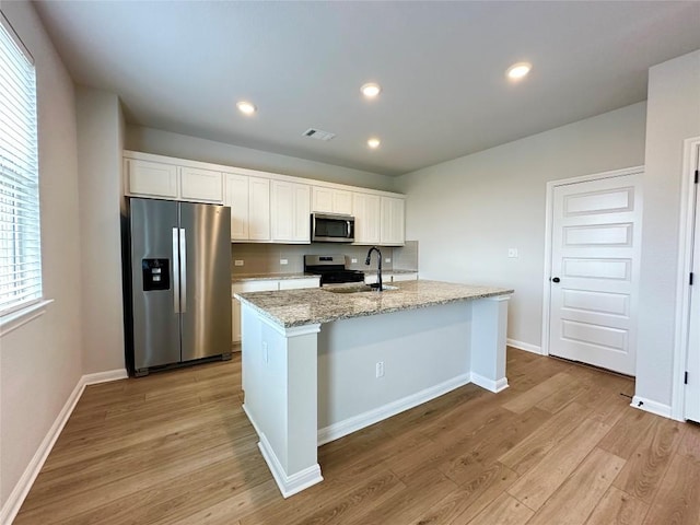 149 Gullivers Dr, Elgin, TX 78621 - kitchen with stainless steel appliances, light wood finished floors, white cabinetry, a center island with sink, and light stone countertops