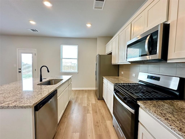 149 Gullivers Dr, Elgin, TX 78621 - kitchen featuring stainless steel appliances, an island with sink, light wood-style flooring, white cabinets, and tasteful backsplash