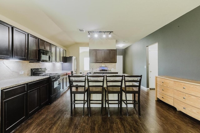 184 Voss St, Kyle, TX 78640 - kitchen featuring black appliances, dark wood-type flooring, tasteful backsplash, a kitchen bar, and lofted ceiling