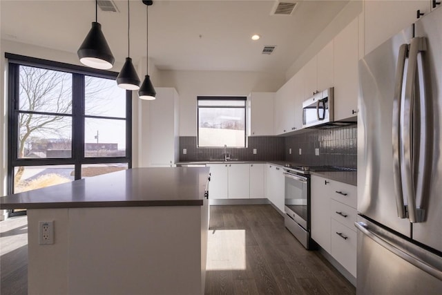 800 Embassy Dr Unit 137, Austin, TX 78702 - kitchen featuring appliances with stainless steel finishes, dark countertops, a center island, backsplash, and white cabinetry