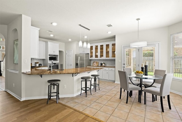 3416 Oxsheer Dr, Austin, TX 78732 - kitchen featuring appliances with stainless steel finishes, a peninsula, tasteful backsplash, a breakfast bar, and glass insert cabinets