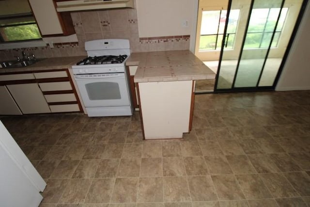 313 Elm St, Copperas Cove, TX 76522 - kitchen with white gas stove, under cabinet range hood, backsplash, a peninsula, and white cabinetry
