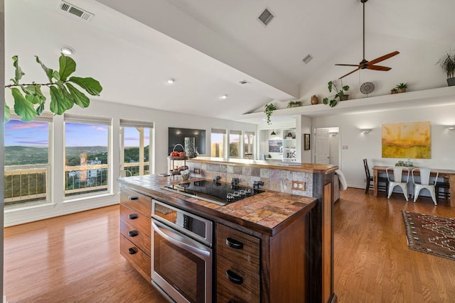 8132 Breeze Way, Jonestown, TX 78645 - kitchen featuring stainless steel oven, black electric cooktop, wood finished floors, ceiling fan, and tile countertops