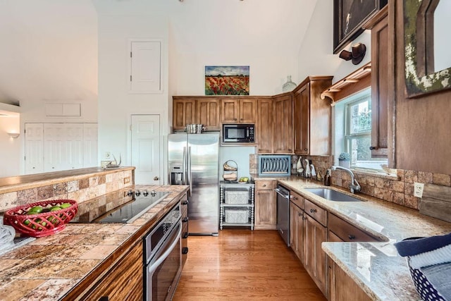 8132 Breeze Way, Jonestown, TX 78645 - kitchen featuring black appliances, a towering ceiling, decorative backsplash, light wood-style floors, and brown cabinetry